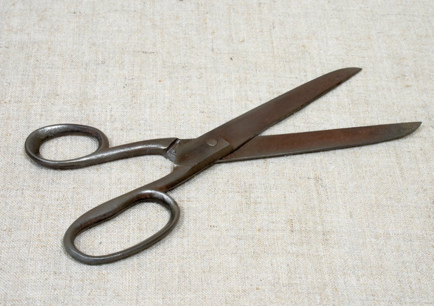 Большие металлические ножницы. Лезвия раскрыты на угол примерно сорок пять градусов, направлены вправо и вверх по диагонали. Кольца для пальцев овальные, массивные, без накладок, оттенок металла тёмно-серый.