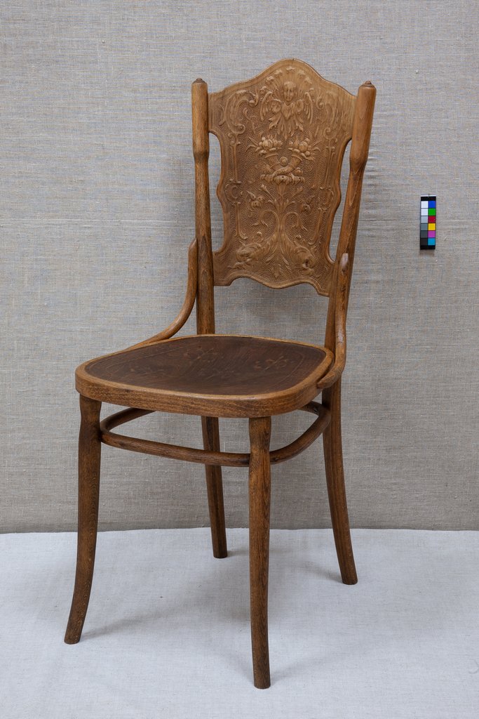 Деревянный стул с высокой резной спинкой и слегка изогнутыми ножками. Спинка украшена сложным растительным орнаментом.