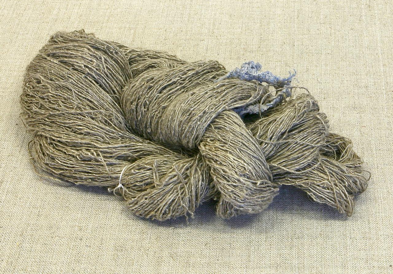Моток серой льняной пряжи без ярких цветов и декоративных элементов. Нити грубые, неравномерные, слегка спутанные