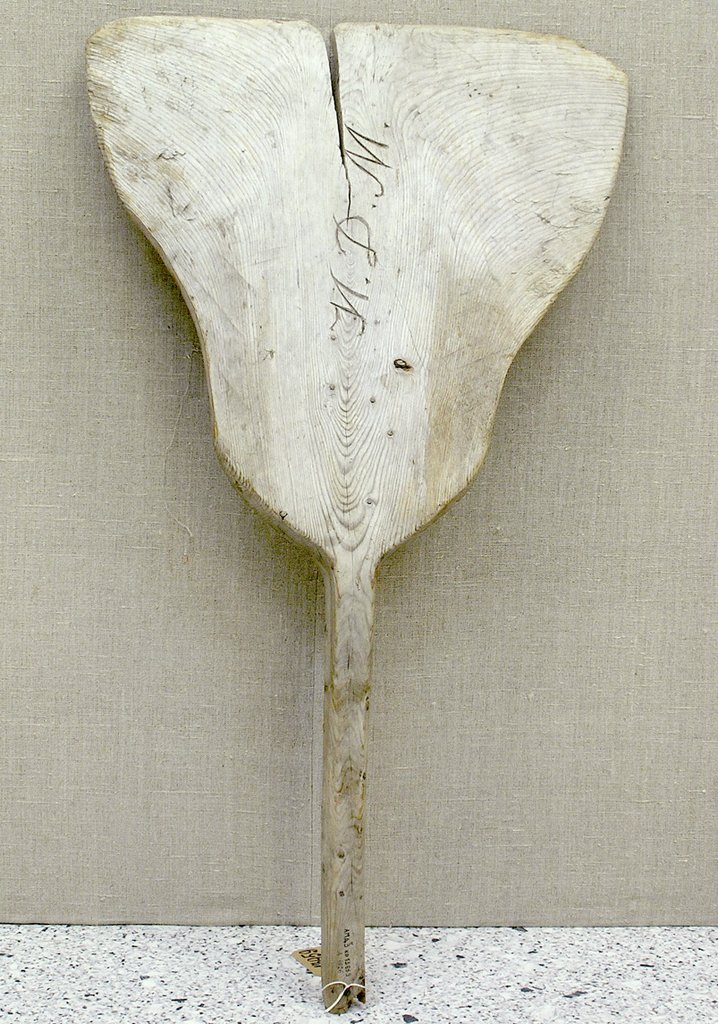 Деревянная лопата с длинной ручкой для уборки снега. На поверхности видны вырезанные инициалы владельца ИДМ. Рабочая часть имеет трещину