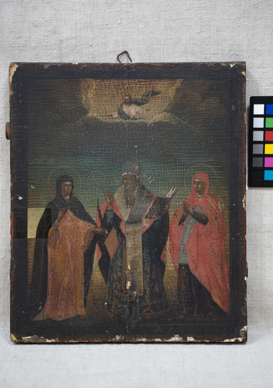 На тёмном фоне изображены три святителя в длинных одеждах, средний в митре с посохом и книгой, по бокам — фигуры с покрытыми головами. Над ними — парящий голубь среди облаков, символ Святого Духа