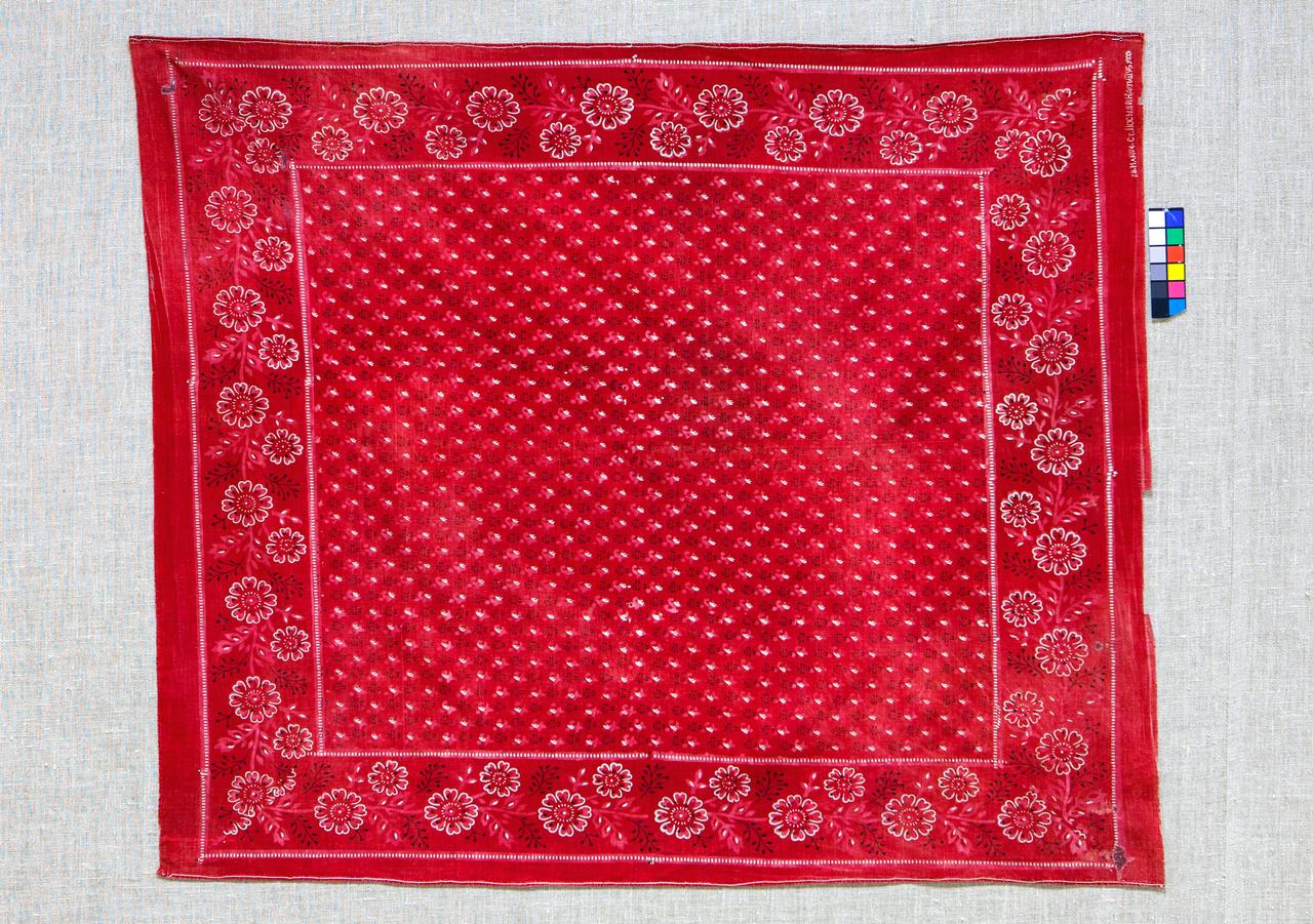 Красный платок с узором из белых и черных цветов и листьев по краю. В центре платка мелкий узор из белых точек