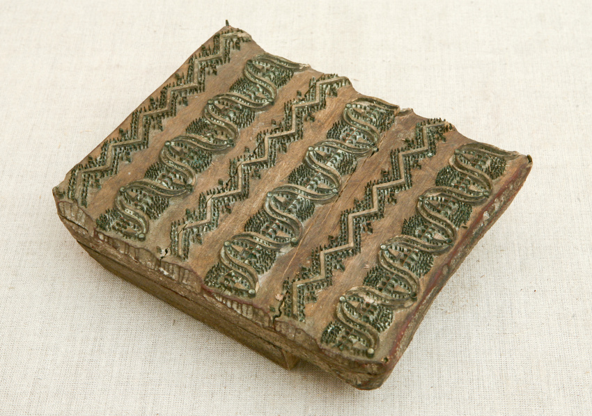 Трёхслойная деревянная форма для печатания на ткани, покрытая рельефным металлическим орнаментом в виде волн и зигзагов.