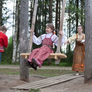 На фотографии девочка в народном костюме качается на качелях