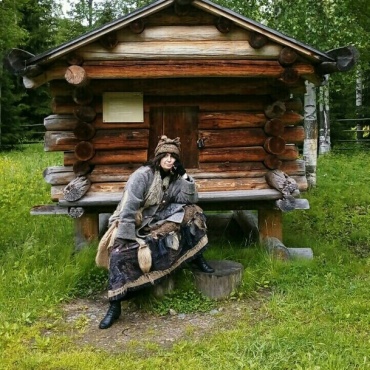 На фотографии изображена колдунья, сидящая на ступеньках деревянного амбара