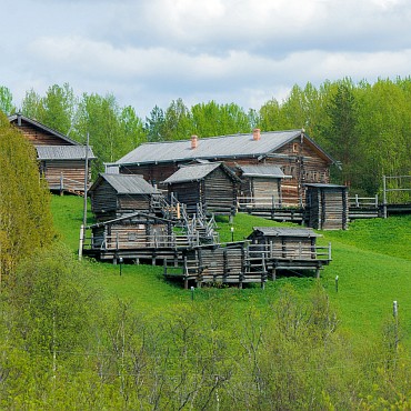 На фотографии летний пейзаж. На переднем плане - хозяйственные постройки. На заднем – ряд деревянных домов