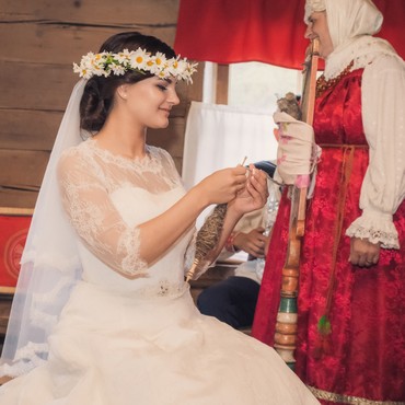 На фотографии изображена невеста в свадебном платье, сидящая за прялкой во время прядения