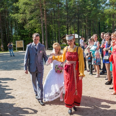 На фотографии девушка в народном костюме ведёт жениха и невесту за полотенце, которым перевязаны их руки