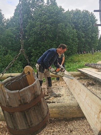 На фотографии изображён плотник, распиливающий бревно бензопилой