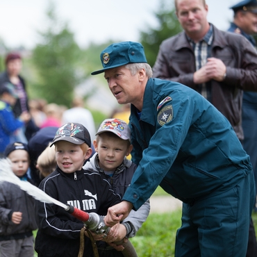 На фотографии пожарный учит детей тушить огонь