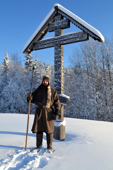 На фотографии изображён мужчина в промысловом костюме помора на фоне креста
