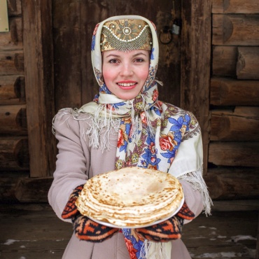 На фотографии девушка в народном костюме держит тарелку с блинами